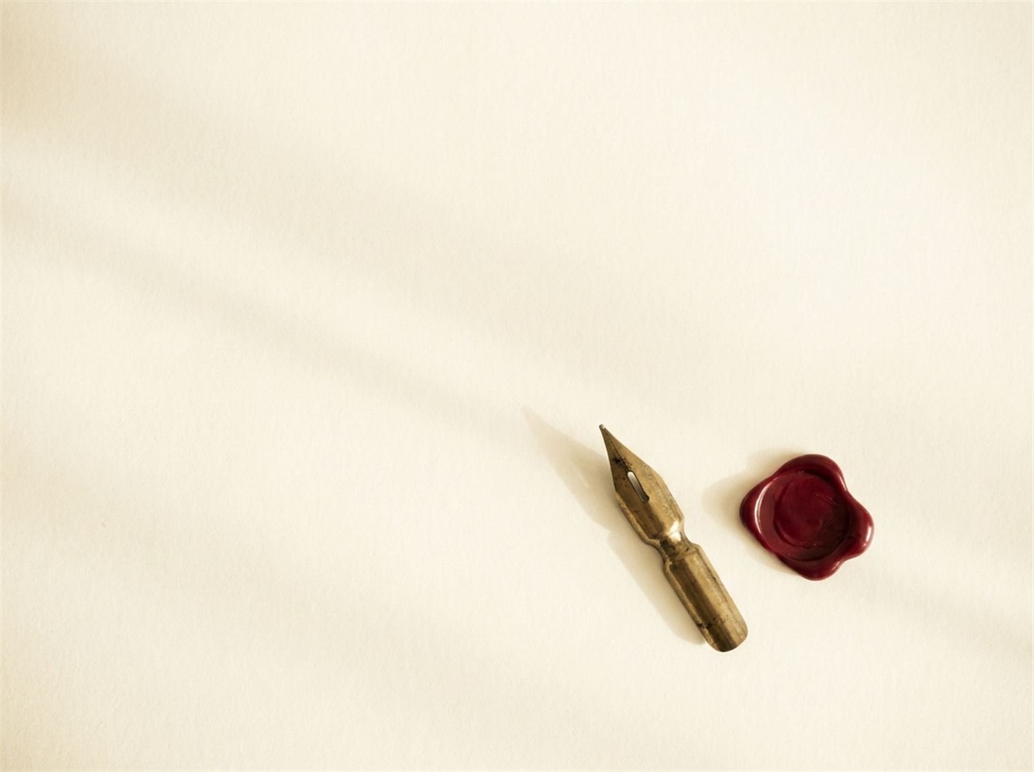 A brass fountain-pen nib and a crimson wax seal resting on warm cream paper